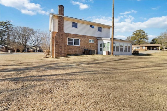 rear view of property with a lawn, central AC, and a sunroom