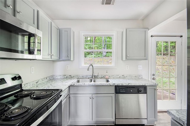 kitchen featuring light stone countertops, a sink, stainless steel appliances, gray cabinetry, and visible vents