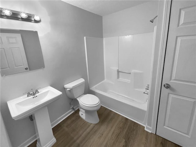 bathroom featuring baseboards, shower / bath combination, toilet, and wood finished floors