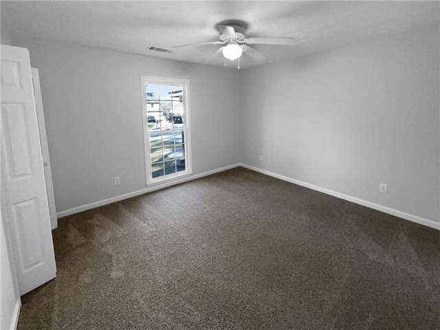 spare room with ceiling fan, dark carpet, visible vents, and baseboards