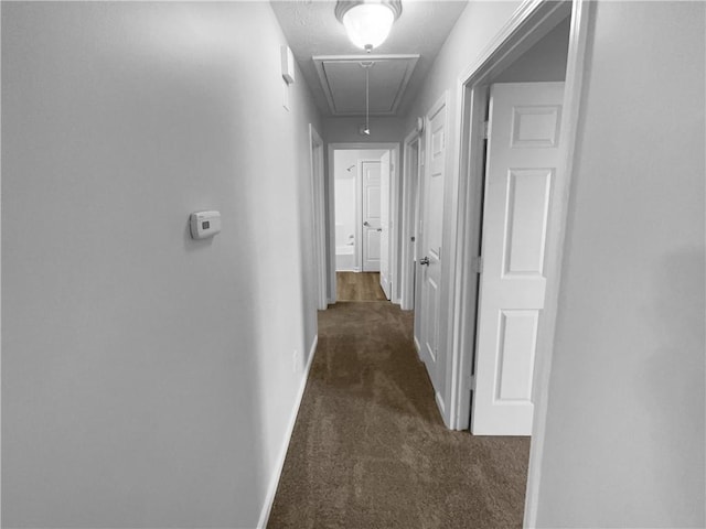 hall with attic access, baseboards, and dark colored carpet