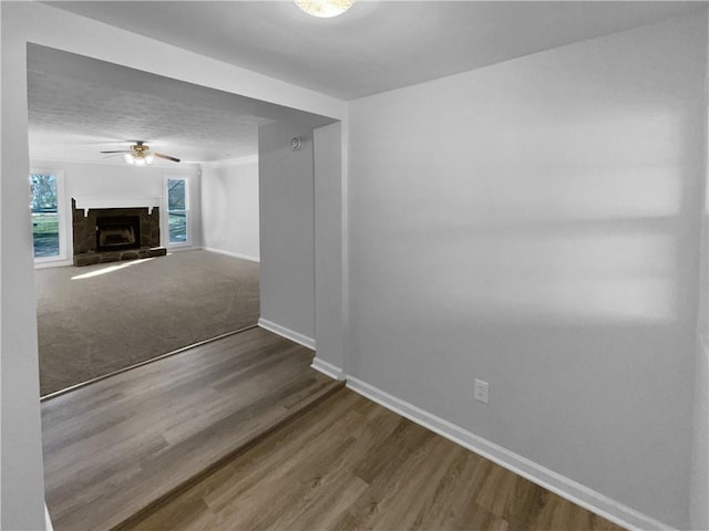 unfurnished living room with ceiling fan, a fireplace, baseboards, and wood finished floors