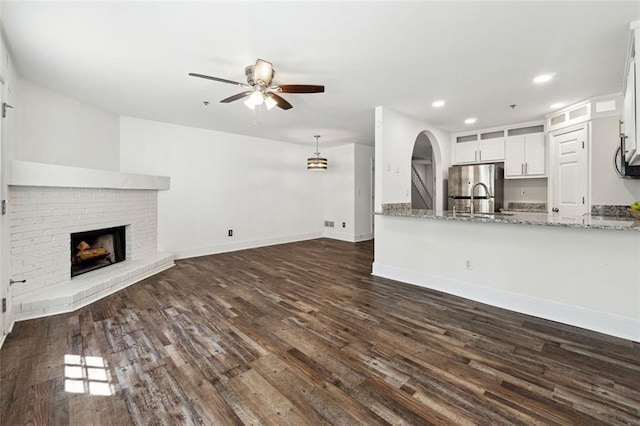 215 Morris Ln, Woodstock, GA 30188 - unfurnished living room featuring a ceiling fan, dark wood-type flooring, a fireplace, arched walkways, and baseboards