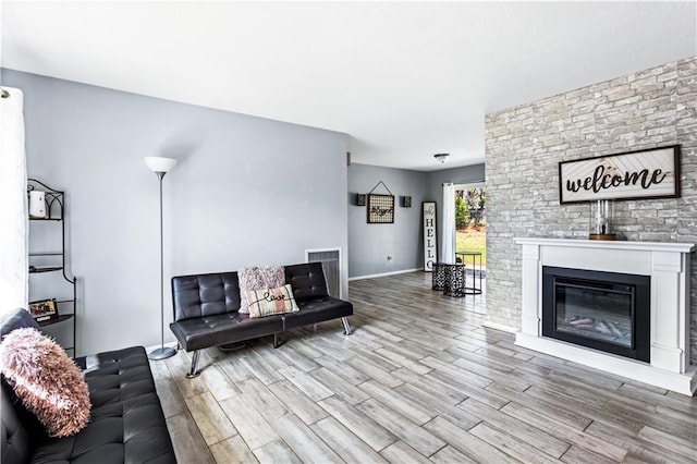 unfurnished living room with light wood-type flooring, a glass covered fireplace, visible vents, and baseboards