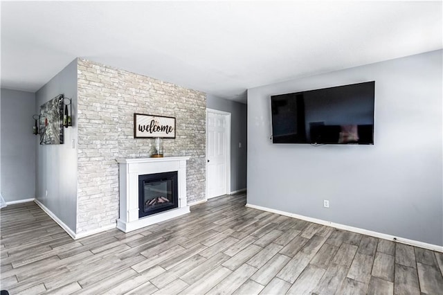 unfurnished living room with light wood finished floors, a glass covered fireplace, and baseboards