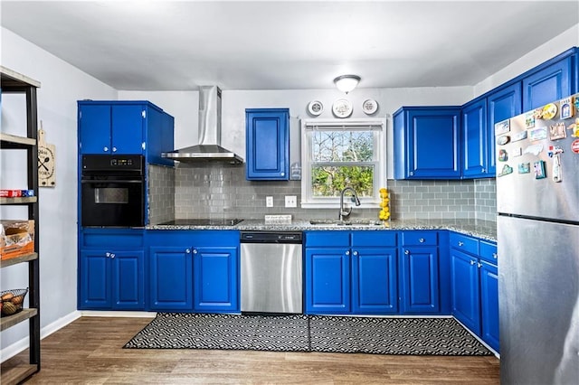 kitchen featuring wall chimney exhaust hood, light stone counters, blue cabinets, black appliances, and a sink