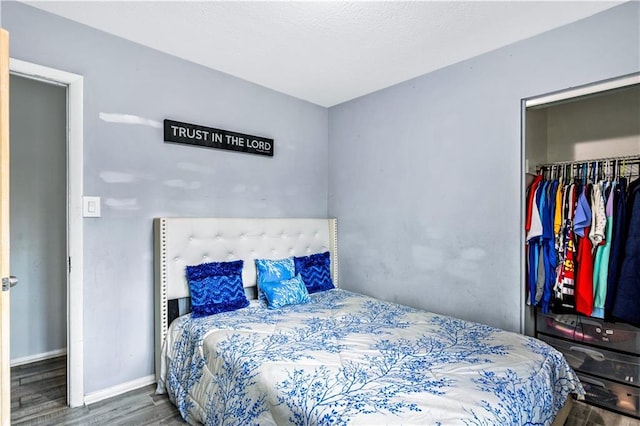 bedroom with a closet, baseboards, a walk in closet, and wood finished floors