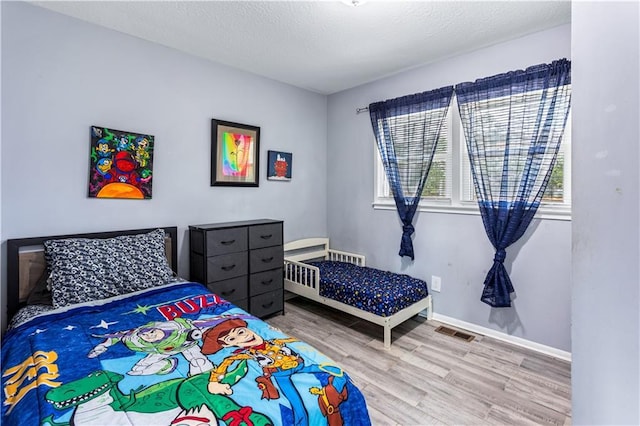 bedroom with a textured ceiling, wood finished floors, visible vents, and baseboards