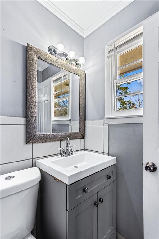 half bath featuring toilet, tile walls, crown molding, and vanity