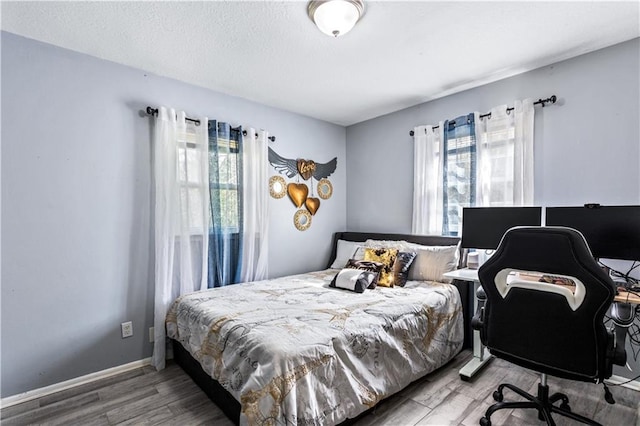 bedroom featuring multiple windows, a textured ceiling, baseboards, and wood finished floors