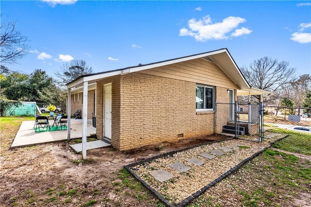 view of property exterior with brick siding, crawl space, a patio area, and fence