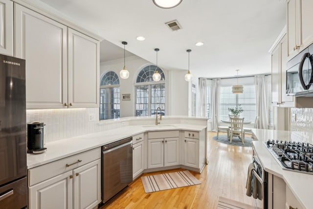 kitchen with white cabinets, appliances with stainless steel finishes, decorative light fixtures, light hardwood / wood-style floors, and sink