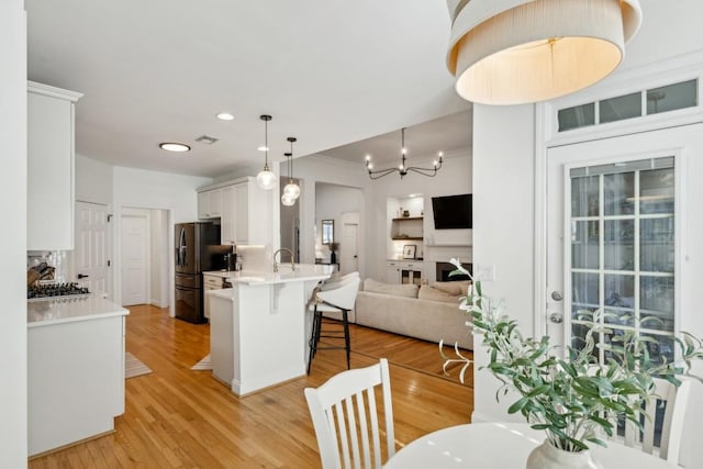 kitchen with black refrigerator with ice dispenser, white cabinetry, kitchen peninsula, pendant lighting, and a breakfast bar area