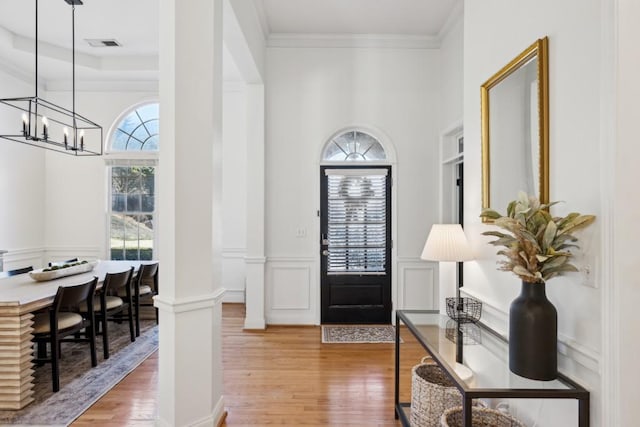 entryway with hardwood / wood-style floors, decorative columns, an inviting chandelier, and ornamental molding