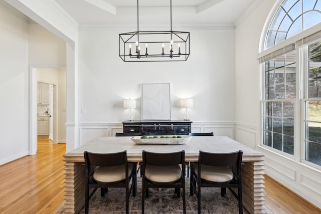 dining room featuring light wood-type flooring, a raised ceiling, crown molding, and an inviting chandelier