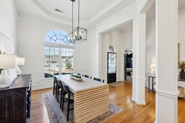 dining space featuring hardwood / wood-style floors, crown molding, a raised ceiling, and ornate columns