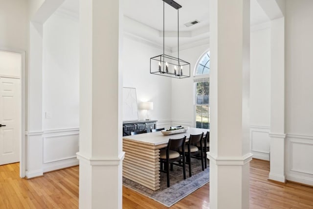 dining space featuring wood-type flooring, ornate columns, an inviting chandelier, a tray ceiling, and crown molding