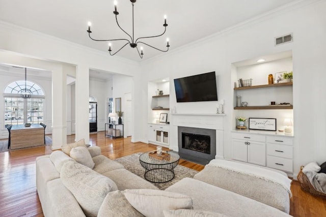 living room with light hardwood / wood-style floors, built in features, crown molding, and a chandelier