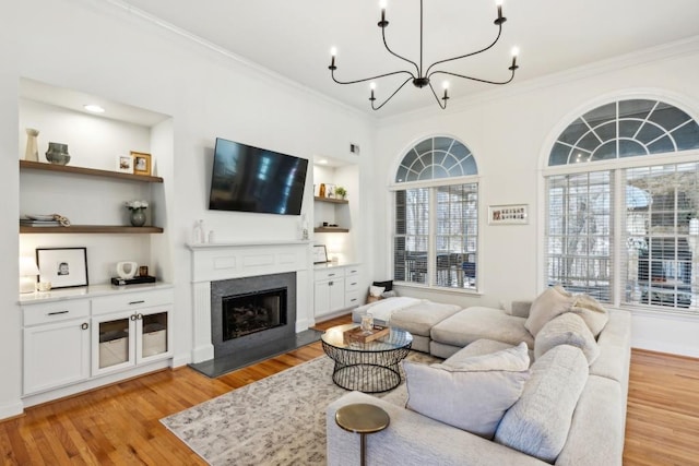 living room featuring built in features, a chandelier, crown molding, and light hardwood / wood-style floors