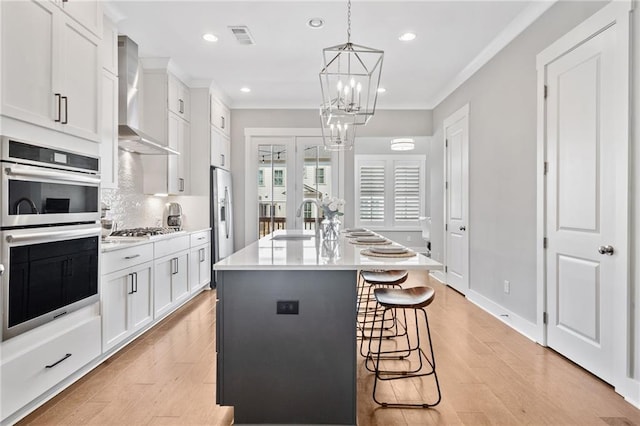 1104 Thomas St, Woodstock, GA 30188 - kitchen with stainless steel appliances, wall chimney range hood, ornamental molding, white cabinets, and light wood-type flooring