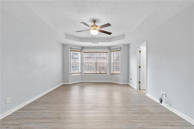 empty room with ceiling fan, light hardwood / wood-style floors, a raised ceiling, and a textured ceiling