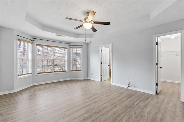 unfurnished room featuring a tray ceiling, light wood-type flooring, a textured ceiling, and ceiling fan