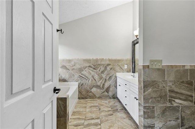 bathroom featuring a bath, a textured ceiling, tile walls, and vanity