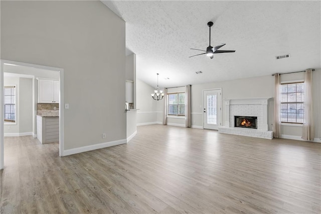 unfurnished living room featuring lofted ceiling, a textured ceiling, ceiling fan with notable chandelier, light hardwood / wood-style floors, and a fireplace