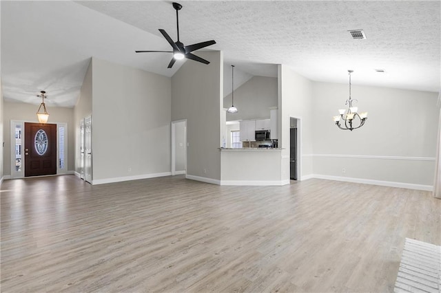 unfurnished living room featuring ceiling fan with notable chandelier, plenty of natural light, light wood-type flooring, and a textured ceiling