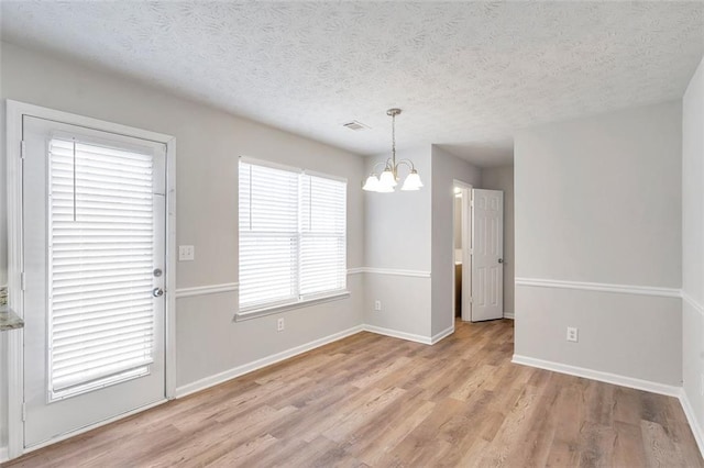 unfurnished dining area featuring a chandelier, light hardwood / wood-style flooring, and a textured ceiling