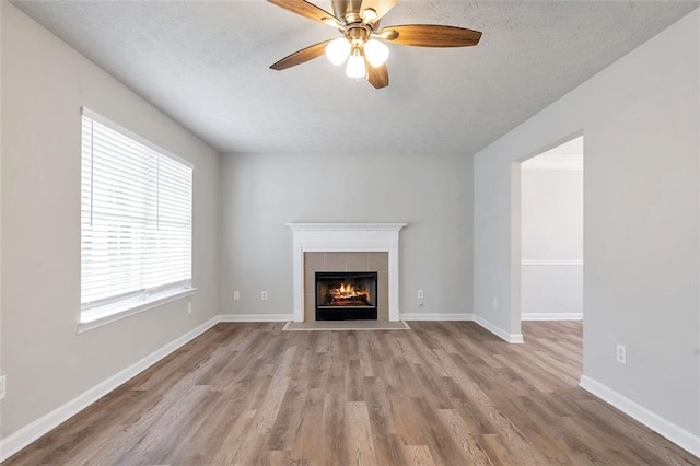 unfurnished living room with ceiling fan, a tiled fireplace, light hardwood / wood-style floors, and a textured ceiling