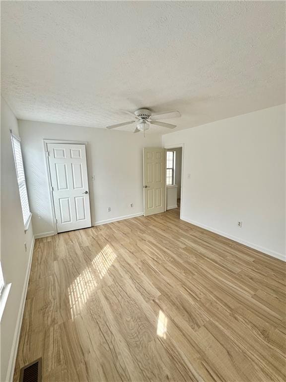 interior space with visible vents, light wood-style flooring, a ceiling fan, a textured ceiling, and baseboards