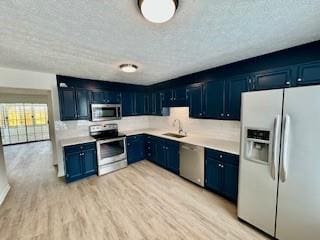 kitchen with light wood finished floors, blue cabinetry, light countertops, appliances with stainless steel finishes, and a sink