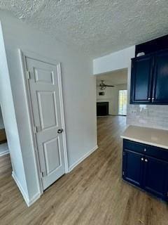 kitchen featuring light wood finished floors, blue cabinets, light countertops, a textured ceiling, and a fireplace