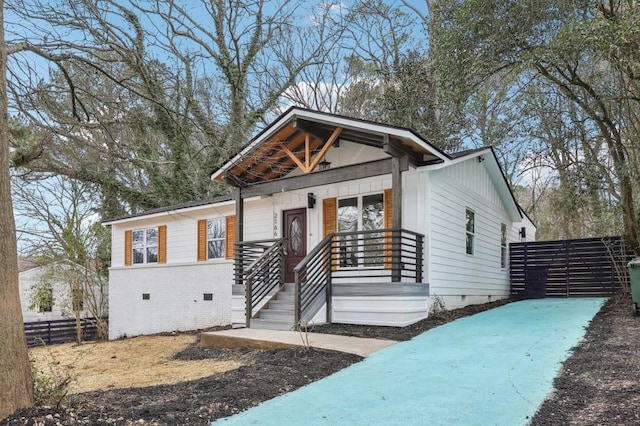 view of front of house featuring covered porch, brick siding, crawl space, and fence