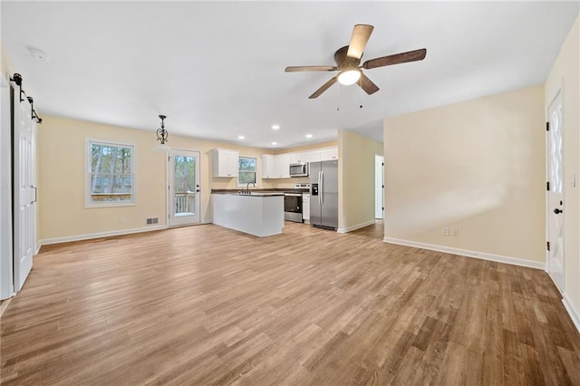 unfurnished living room with ceiling fan, a barn door, light wood-type flooring, and sink