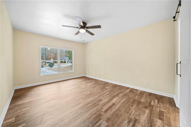 empty room with hardwood / wood-style flooring, ceiling fan, and a barn door