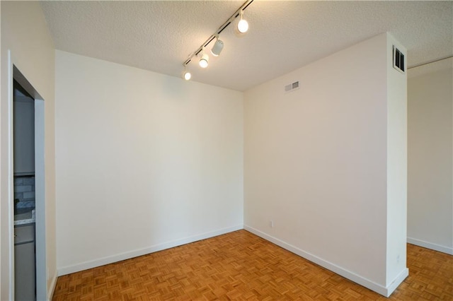 spare room with light parquet floors, track lighting, and a textured ceiling