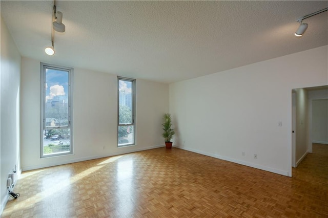 empty room featuring rail lighting, a textured ceiling, and light parquet floors