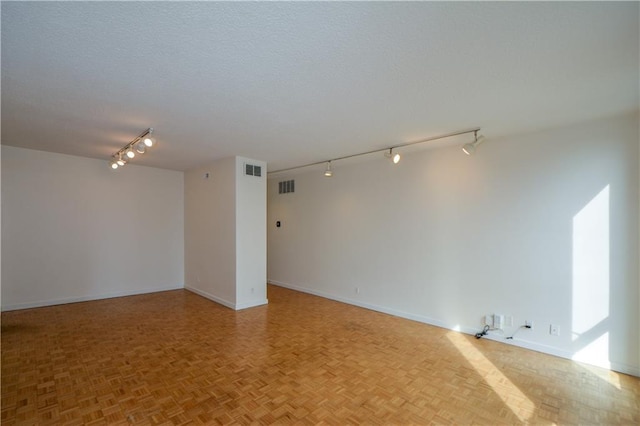 spare room featuring light parquet floors, rail lighting, and a textured ceiling