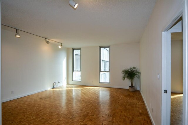 spare room with dark parquet flooring, rail lighting, and a textured ceiling