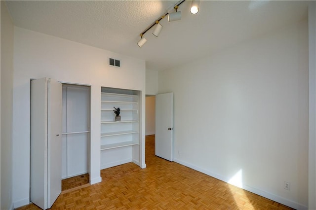 unfurnished bedroom featuring a closet, rail lighting, a textured ceiling, and light parquet floors