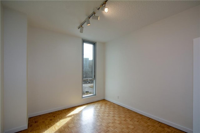 spare room with a textured ceiling, rail lighting, and light parquet flooring