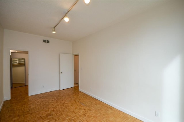 unfurnished bedroom with a walk in closet, track lighting, a closet, and light parquet floors