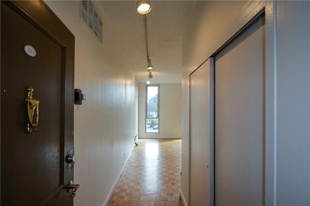 hallway featuring a textured ceiling, rail lighting, and light parquet floors