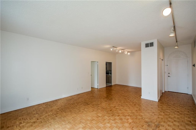 spare room featuring light parquet floors, rail lighting, and a textured ceiling