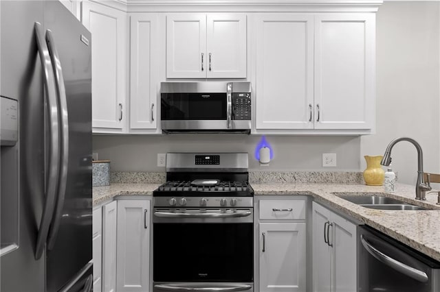 kitchen with a sink, stainless steel appliances, light stone counters, and white cabinets