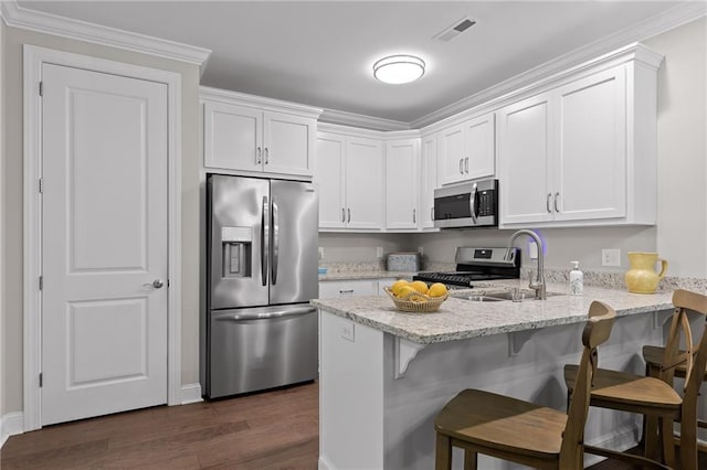 kitchen featuring visible vents, a peninsula, stainless steel appliances, white cabinetry, and a sink