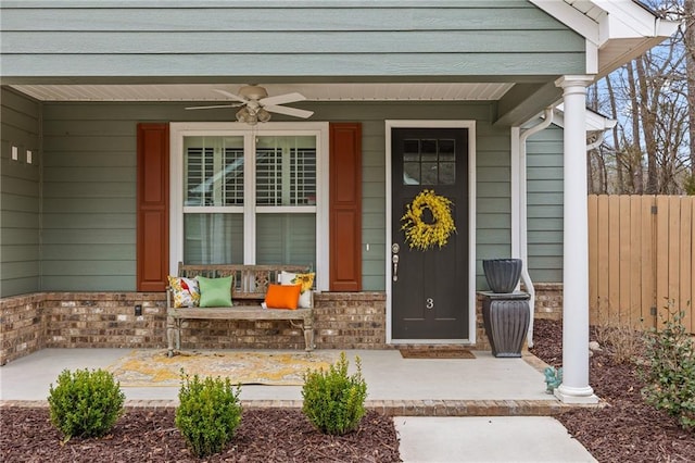 doorway to property with brick siding, a porch, a ceiling fan, and fence