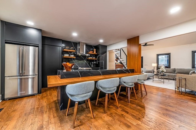 kitchen with a breakfast bar area, wood-type flooring, tile counters, stainless steel fridge, and kitchen peninsula